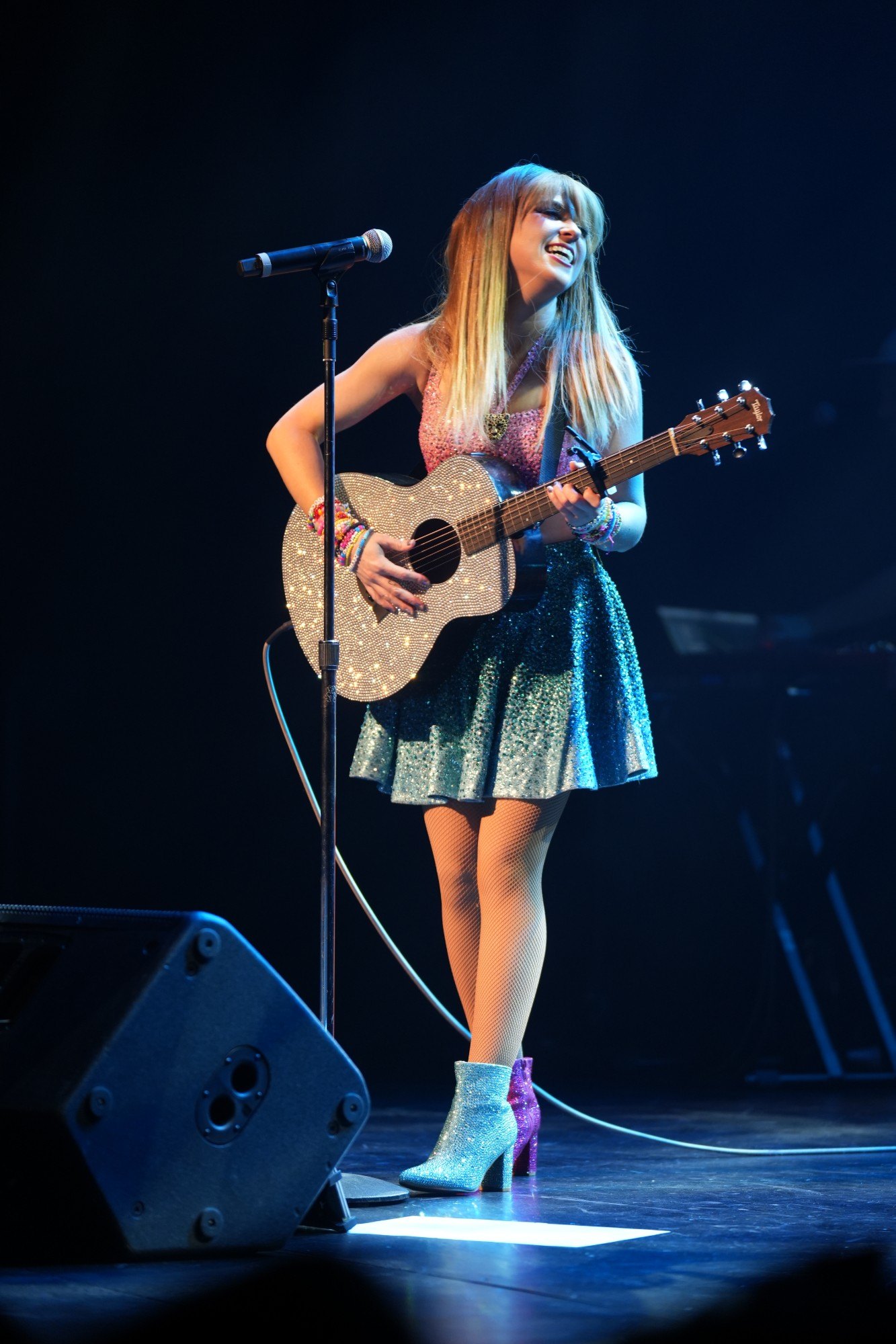 Melody Ebner singing and playing a rhinestone acoustic guitar on stage