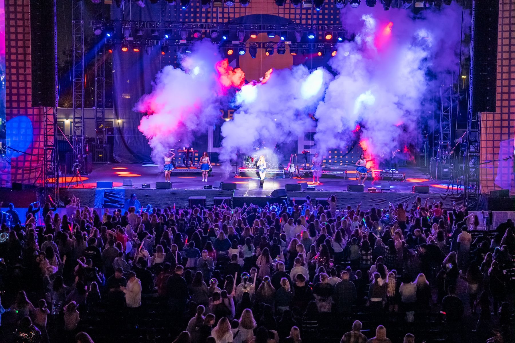 Smoke jets fire on stage as dancers perform for a packed crowd